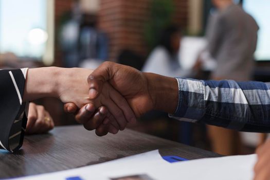 Close up of applicant shaking hand with african american businessman during interview meeting in startup business company office. Executive manager hiring employer while sitting at desk.