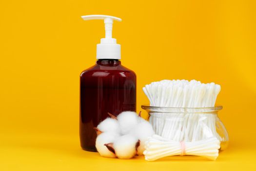 Liquid soap, cotton ear sticks and cotton flower on yellow background