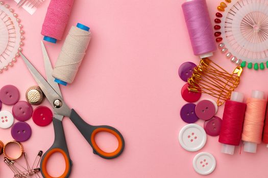 Sewing accessories including thread spools and pins on pink background