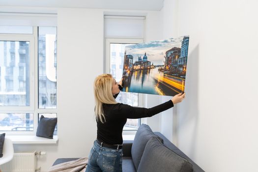 Canvas print with gallery wrap. Woman hangs photography on white wall. Hands holding photo canvas print.