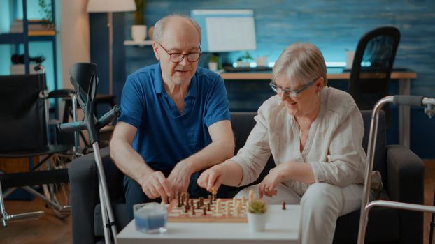 Elder couple with walk frame and crutches playing chess game