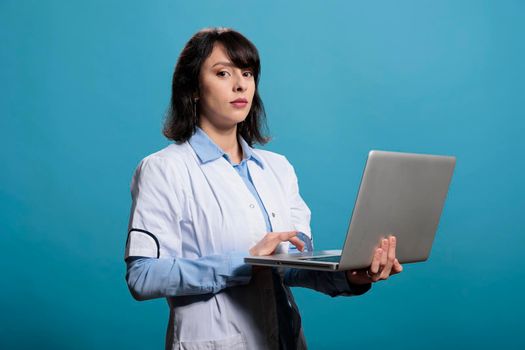 Biochemistry scientist standing on blue background having modern computer laptop while looking at camera.