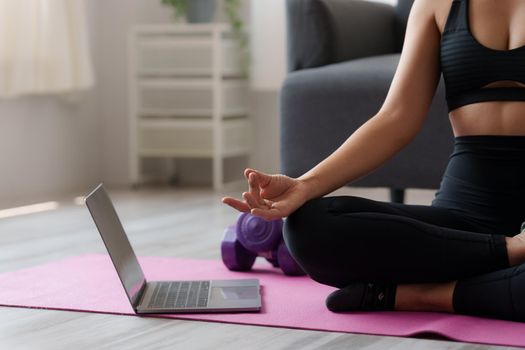 Young woman practicing yoga follow teacher in laptop online class at home. Calmness and relax concept.