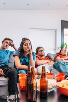 sad friends watching TV because their football team lost the game. upset young people at a house party.