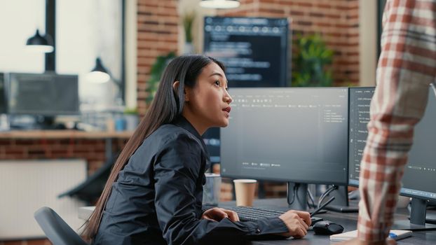 Database developer pointing pencil at computer screen with software compiling code explaining source algorithm to coworker