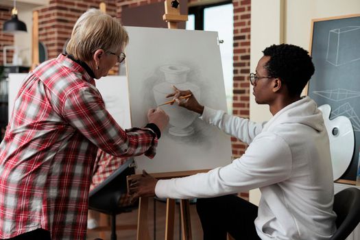 Senior teacher explaining sketching technique to african american student