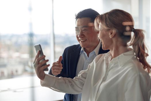 mature businesswoman is showing to her exited partner screen of smartphone in modern office