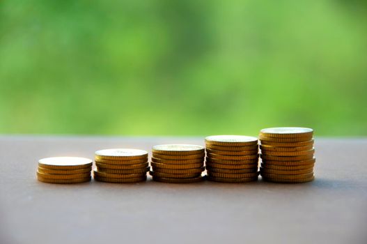 Gold coins stacked on wooden table with blurred nature background.