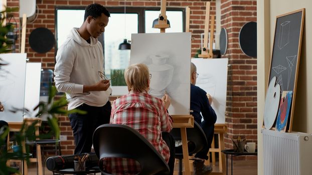 Male teacher giving advice to elder woman in drawing class