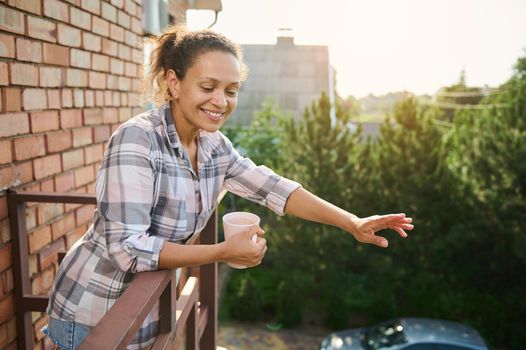 Smiling Hispanic woman on the balcony of a country house, enjoying coffee break