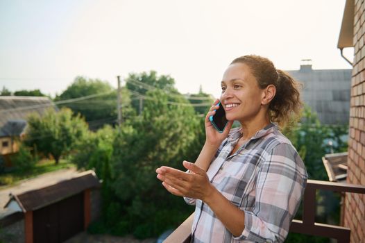 Pleasant African American woman standing on balcony and talking on mobile phone