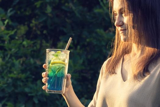 Young woman with long dark hair holds a summer refreshing cocktail in her hand. Selective focus