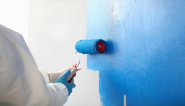Painter with brush tool covered in blue colour painting wall
