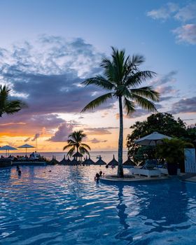 sunset by a swimming pool with tropical palm trees during a luxury vacation holiday