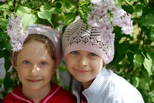 Two little girls-girlfriends by the lilac bush and smiling.