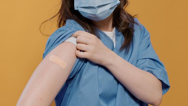 Closeup of medical doctor wearing surgical mask lifting sleeve and showing band aid after covid or flu vaccine
