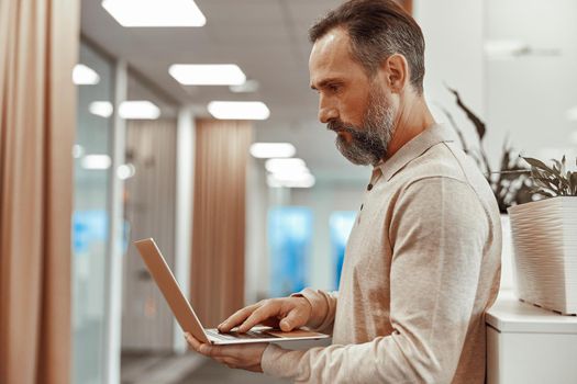 Caucasian bearded male office worker is holding laptop
