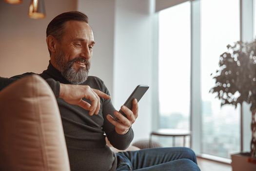Happy bearded man sitting and typing message on mobile phone