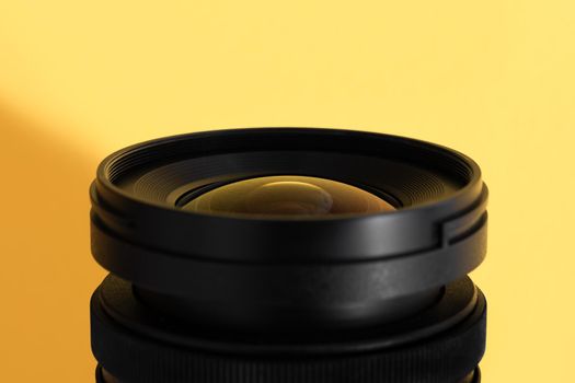 Close-up of an wide angle camera lens with glass reflections on yellow background