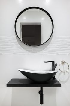 White tiled bathroom with black faucet and basin and round mirror. Modern and minimalist style.