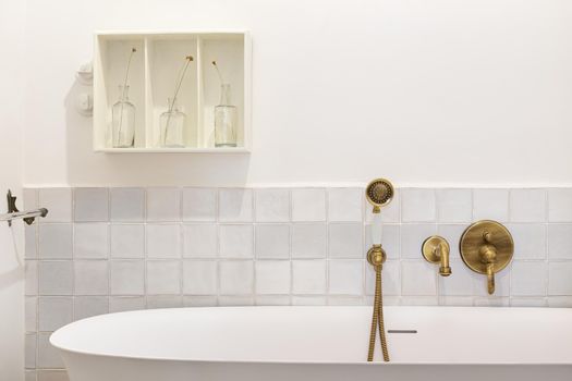 Retro style bathroom decorated in white with bathtub and vintage faucet and shower head of bronze color.