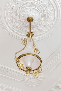 Vintage chandelier in the interior of white room with stucco molding on the ceiling