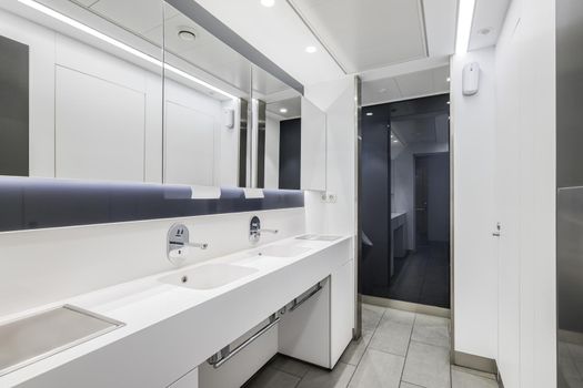 Public or office interior of male restroom with sinks and big mirror. Modern design bathroom in white color.