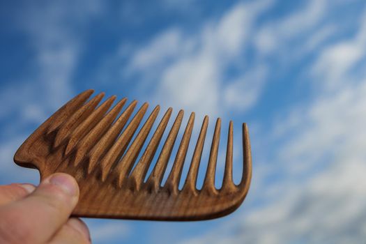 Handmade wooden comb for scalp massage and hair combing at blue sky background. Hair care concept.