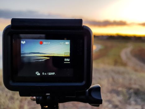 An action camera shooting the time-lapse of the sunset in the meadow near the estuary in early autumn.