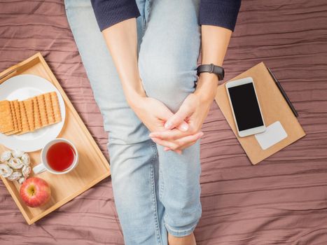 Flatlay of woman in jeans sitting on her bed hugging her knees, with smartphone