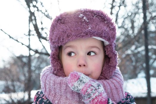 Winter, games, family, childhood concepts - close-up portrait authentic little preschool minor 3-4 years girl in pink hat look at camera posing smiles in snowy frosty weather. Funny kid eat taste snow