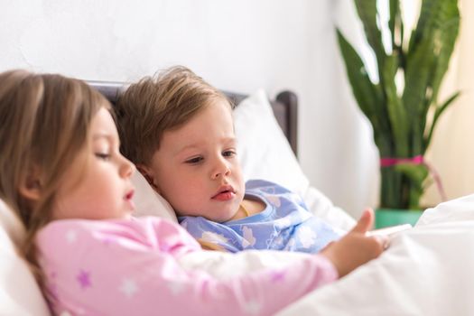 Little Preschool Toddler Minor Children Siblings Kids Watch Cartoon Use Smartphone Phone Device Together. Baby In Pajama On White Bed At Home Bedroom. Family, Leisure, Childhood, Friendship Concept