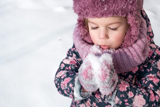 Winter, games, family, childhood concepts - close-up portrait authentic little preschool minor girl in pink hat warm clothes have fun smiles in cold frosty weather day. Funny kid blow on white snow