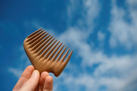 A hand holding natural wooden comb made of pear tree for scalp massage and aroma combing