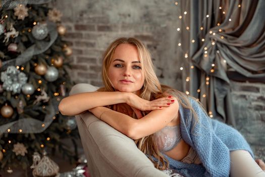 A young blonde woman is sitting on the sofa. The room is decorated with a Christmas tree.