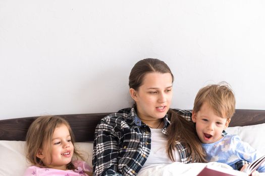 happy family. Close up loving mother lying with daughter son two kids pajamas in bed children reading interesting storybook, preschool smiling kid girl enjoy fairytale before go to sleep good pastime