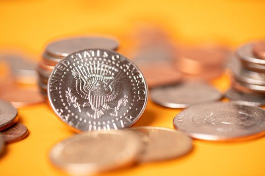 US dollar coins on orange background. Half dollar coins piled up with pennies and quarters. Dollar currency stacked and piled up