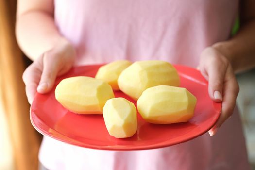 Female hands holding plate with raw peeled potatoes on it
