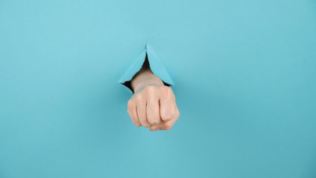 A woman's hand sticking out of a hole from a blue background shows a fist.