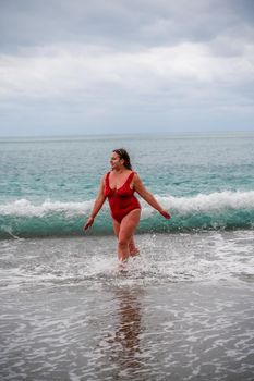 Woman in a bathing suit at the sea. A fat young woman in a red swimsuit enters the water during the surf