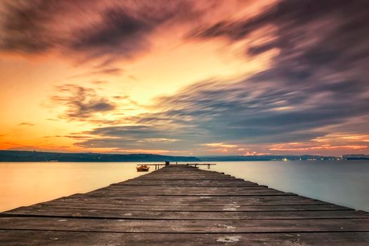 Exciting sky with clouds at the shore with wooden pier and boat