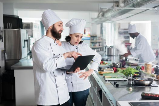 Sous chef with modern laptop recommending dinner dish service recipe to head chef