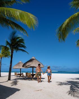 Tropical beach with palm trees and white sand blue ocean and beach beds with umbrella,Sun chairs and parasol under a palm tree at a tropical beac, Le Morne beach Mauritius