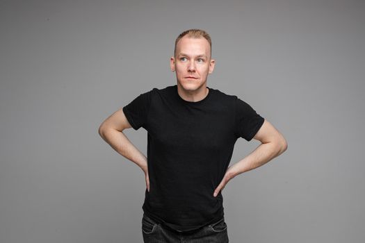 attractive man with short fair hair wearing a black t-shirt and jeans keeps hands on the belt