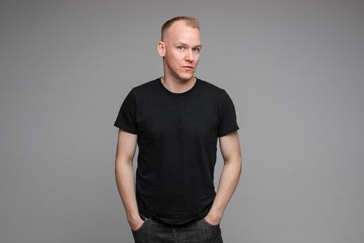 attractive man with short fair hair wearing a black t-shirt and jeans looks aside with surprised sight