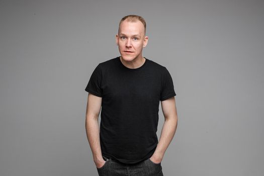 attractive man with short fair hair wearing a black t-shirt and jeans looks aside with surprised sight