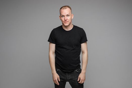 adult man with short fair hair wearing a t-shirt and jeans keeping hands down with tired face