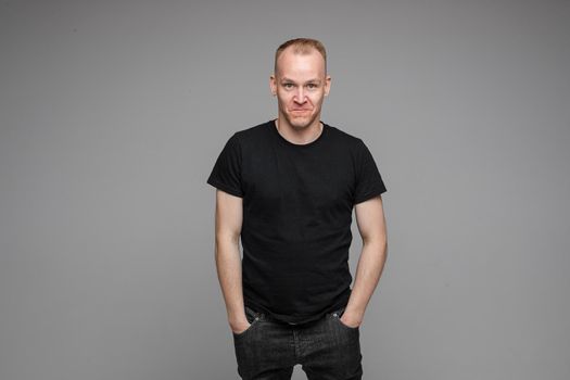 attractive man with short fair hair wearing a black t-shirt and jeans keeping hands in pockets and smiling