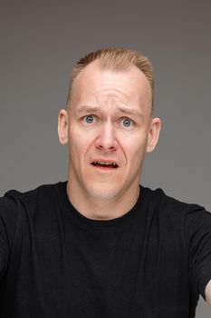 portrait of caucasian male in black t-shirt looks at something disgust isolated on grey background