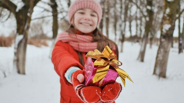The charming young schoolgirl joyfully holds in her hands a packaged box with a gift in the winter forest. In anticipation of the New Year holidays.
